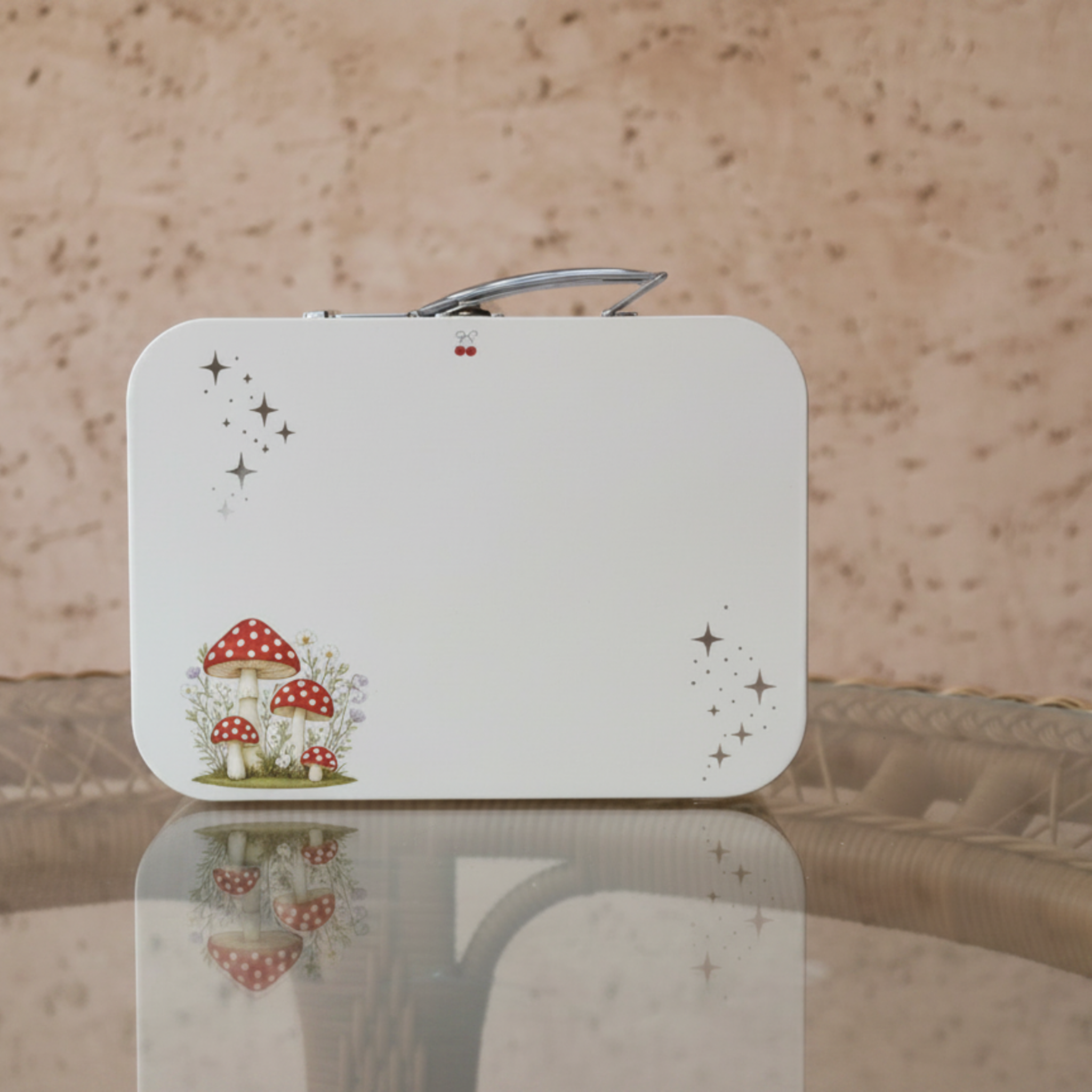 Sleepy softie keepsafe box with rounded corners, featuring a small illustration of red-and-white mushrooms and star accents near the bottom left, standing on a reflective surface against a textured beige background.