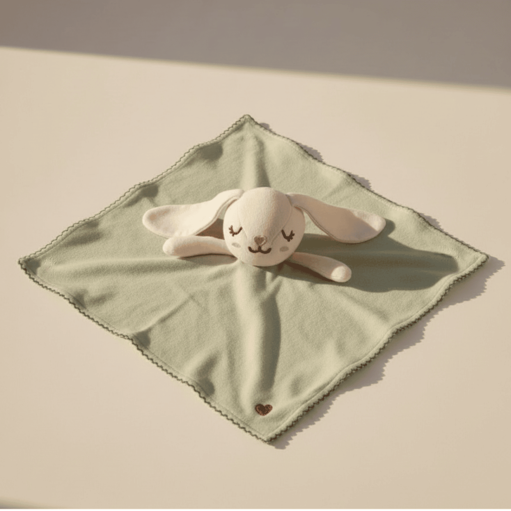 Pink bunny plush toy on a green blanket with a heart detail on a beige background