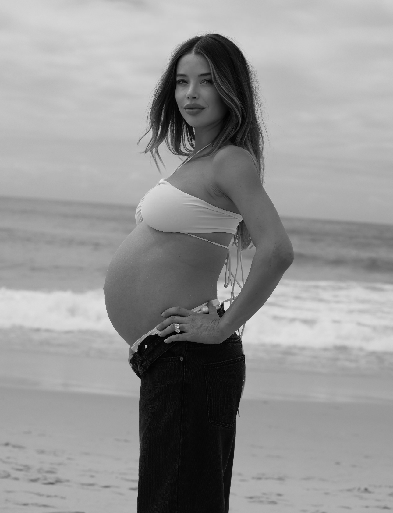 Pregnant woman standing on a beach with ocean waves in the background