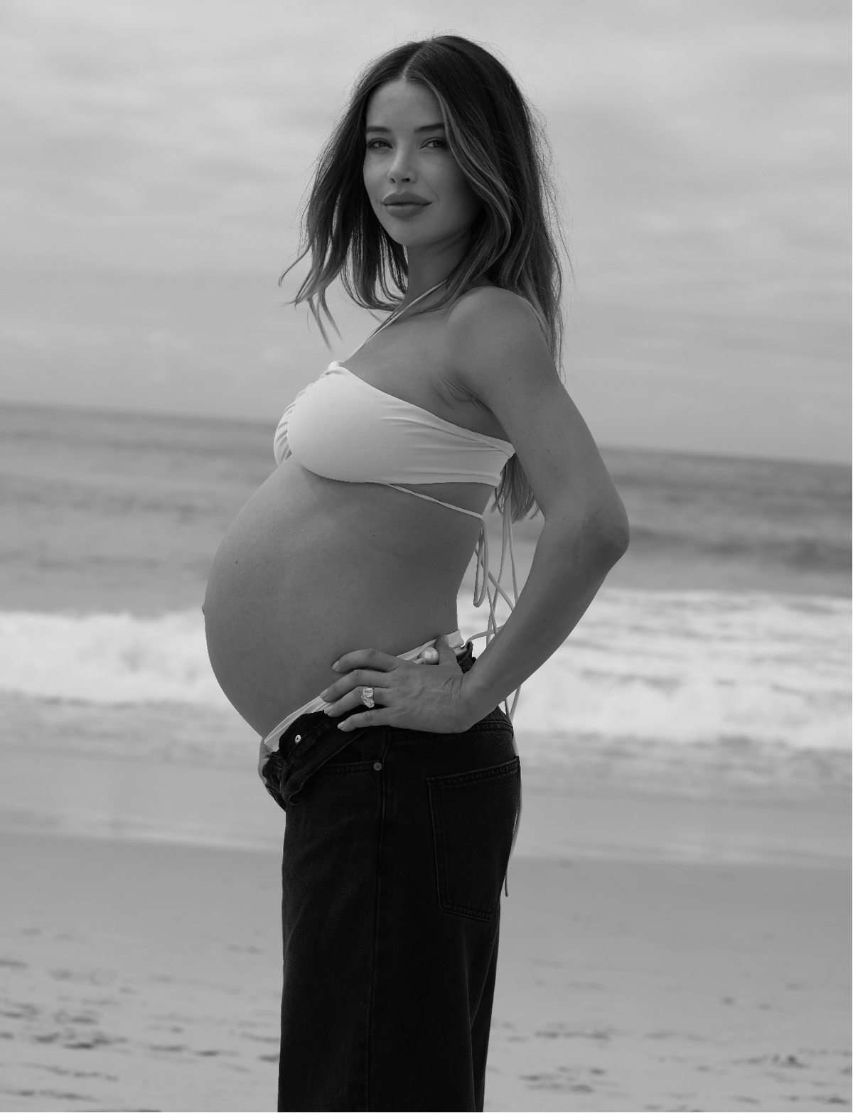 Pregnant woman standing on a beach with ocean waves in the background