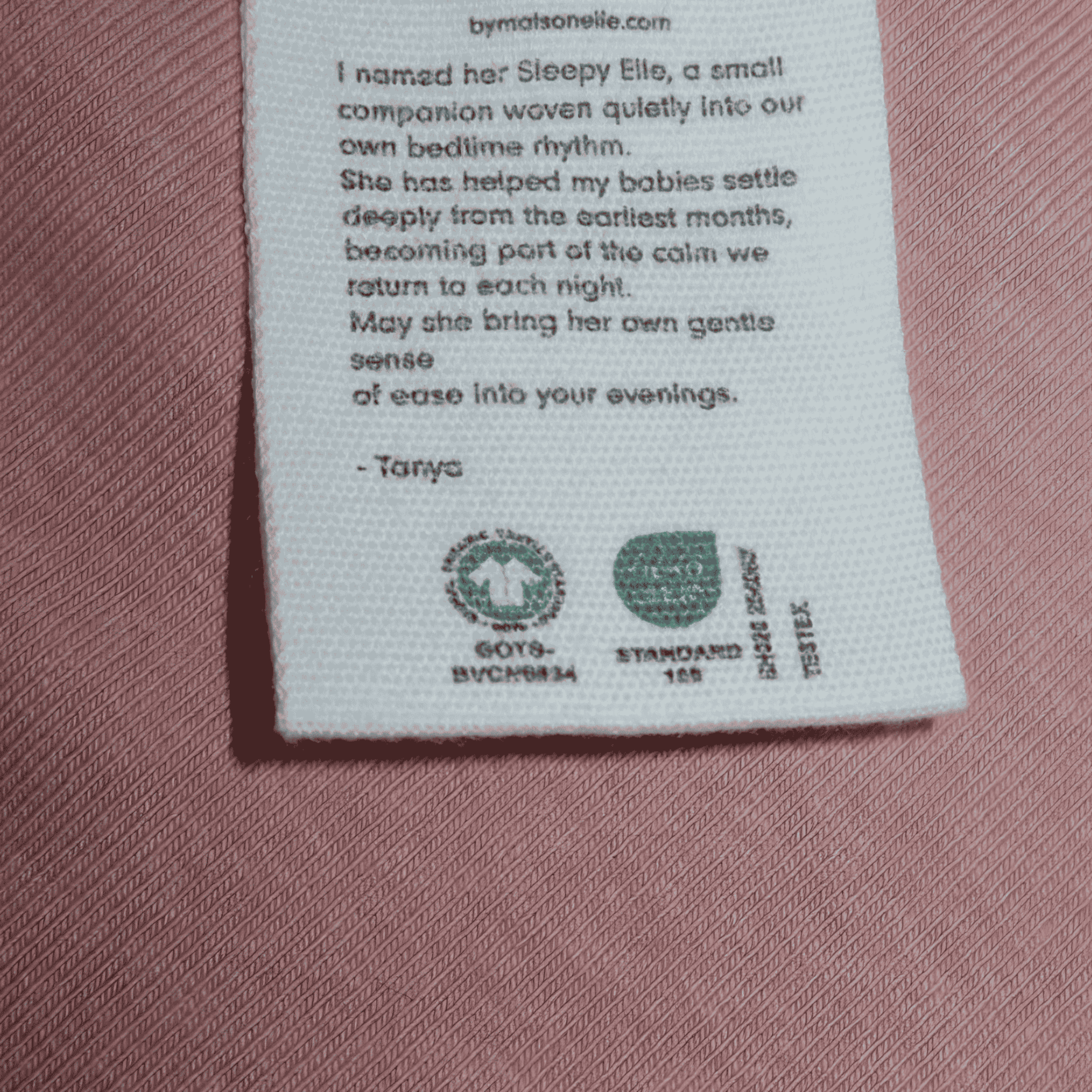 Text label on a pink fabric background with branding and text.