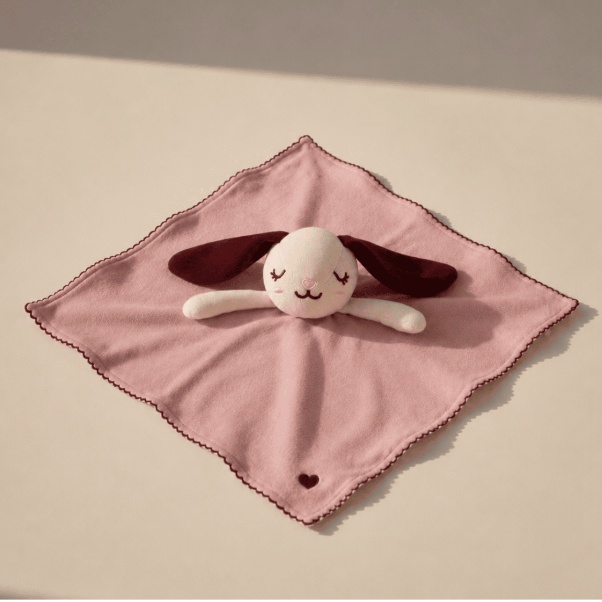 Plush toy with closed eyes on a pink blanket against a beige background