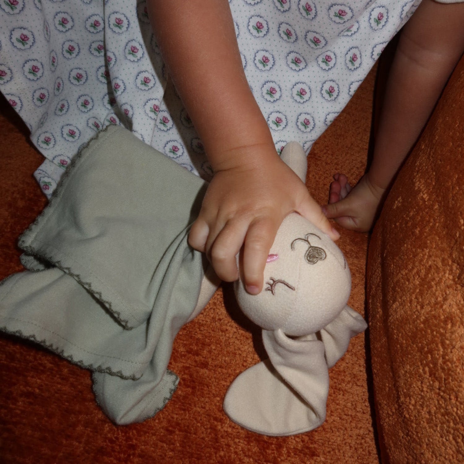 Close-up of baby hand holding Maison Elle Organic Sleep Softie in sage green organic cotton