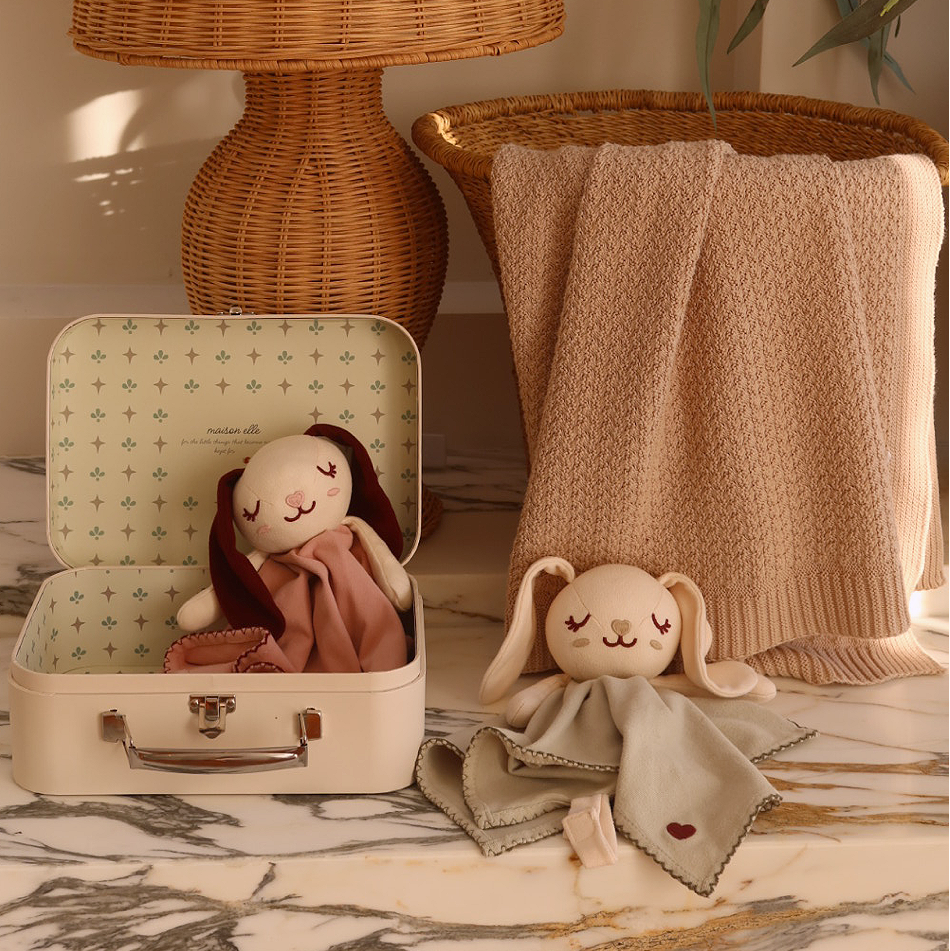 sleepy elle organic cotton baby comforters in dusty pink and sage green beside an open maison elle keepsake suitcase